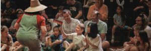 An audience of young children and families smiling at a performer on stage.