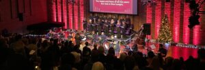 A choir and musicians on stage with a Christmas tree. The audience are standing.