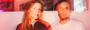 A blurred image of a man and a woman sat beside each other gazing at the camera