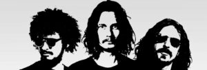 Three men with long hair stand together in black and white.