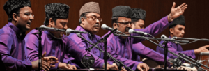 Six men sit next to each other with microphones in front of them.