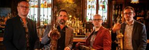 Four men sat in front of a bar holding saxophones