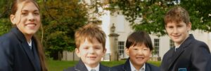 Four children wearing a black school uniforms are sitting together and smiling.