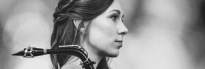 A woman with long hair holds a saxophone at profile view.