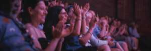 An audience are sat in Turner Sims' main auditorium, clapping and smiling.