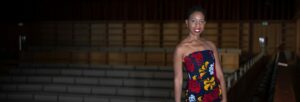 A woman stands in a dark concert hall wearing a black jumpsuit with red and yellow patterns.