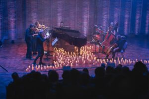 A classical ensemble on stage surrounded by candles with an audience looking on