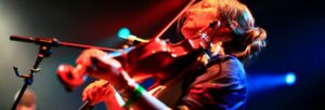 A woman under stage lights playing a fiddle