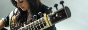 A close up image of an Indian woman with long dark hair playing a sitar