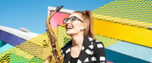 A young woman with a ponytail holding a saxophone laughing with a brightly coloured background and blue sky - with yellow abstract wiggly lines running behind her