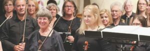 A group of women wearing black and holding string instruments on a stage with music stands