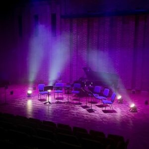 A stage set with chairs and a grand piano, lite with purple stage lights