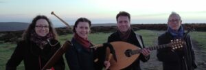4 people standing outside on a hill wearing coats and scarves holding folk instruments.