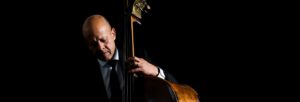 A man lit against a dark backgroung, wearing a suit and playing a double bass