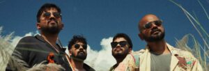 Four men, all wearing dark glasses, stood against a blue sky