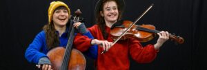 Two women in bright jumpers and hats playing string instruments