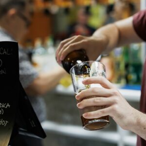 A close up shot of a person pouring a bottle of beer into a pint glass