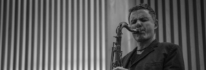 Black and white image of a man playing a saxophone wearing a dark suit