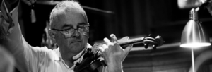 A black and white image of a man wearing glasses and a white shirt playing the violin.