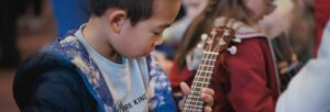 A small boy playing a ukulele